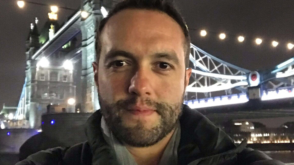 Male student smiling at the camera with a lit-up bridge in the background at night.