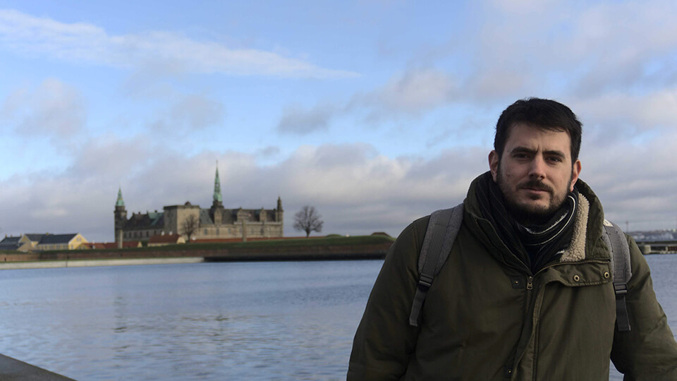 Male student wearing a scarf and a winter jacket outside in front of a historic building.