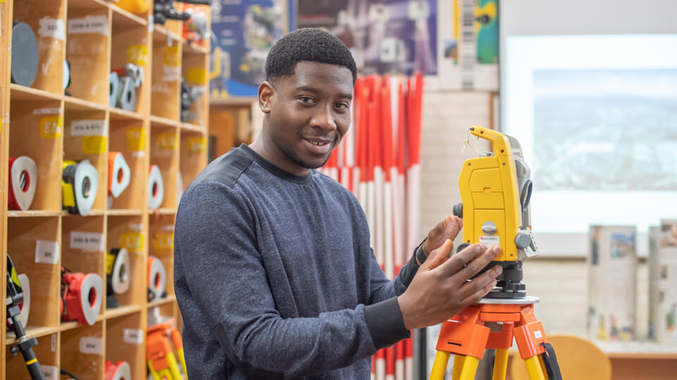 Male student smiling to the camera next to surveying equipment.