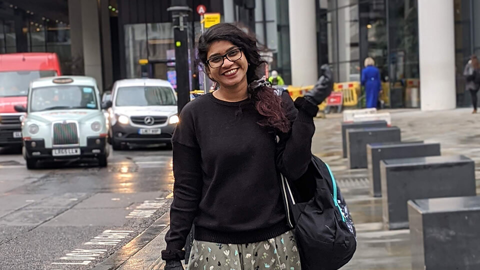 Female student in a black jumper standing on a street in London, smiling at the camera.