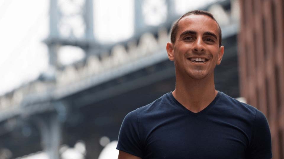 Male student smiling at the camera with a bridge in the background.