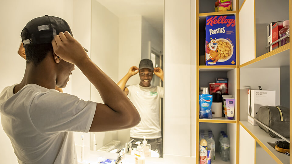 Male student in his bathroom at his student halls, looking in the mirror and smiling.