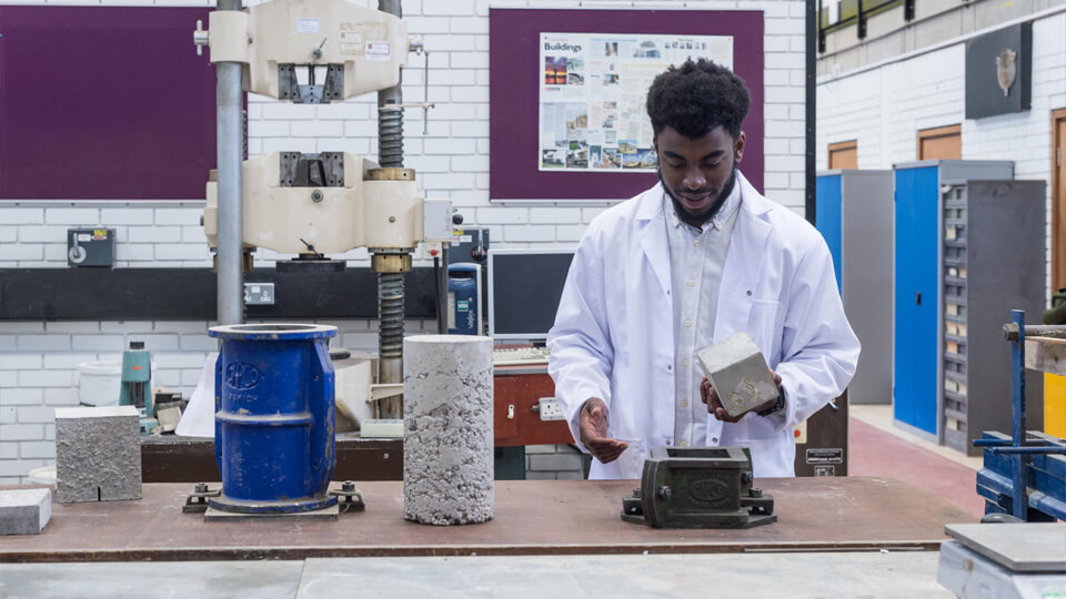 Male researcher in a white lab coat doing testing in a lab using a concrete cube.