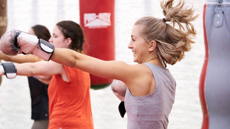 People in a boxing gym punching a bag with boxing gloves on