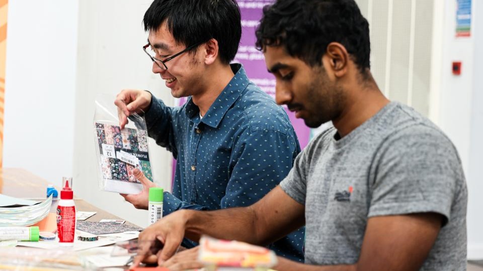 Two people sat down at a table making bookmarks.