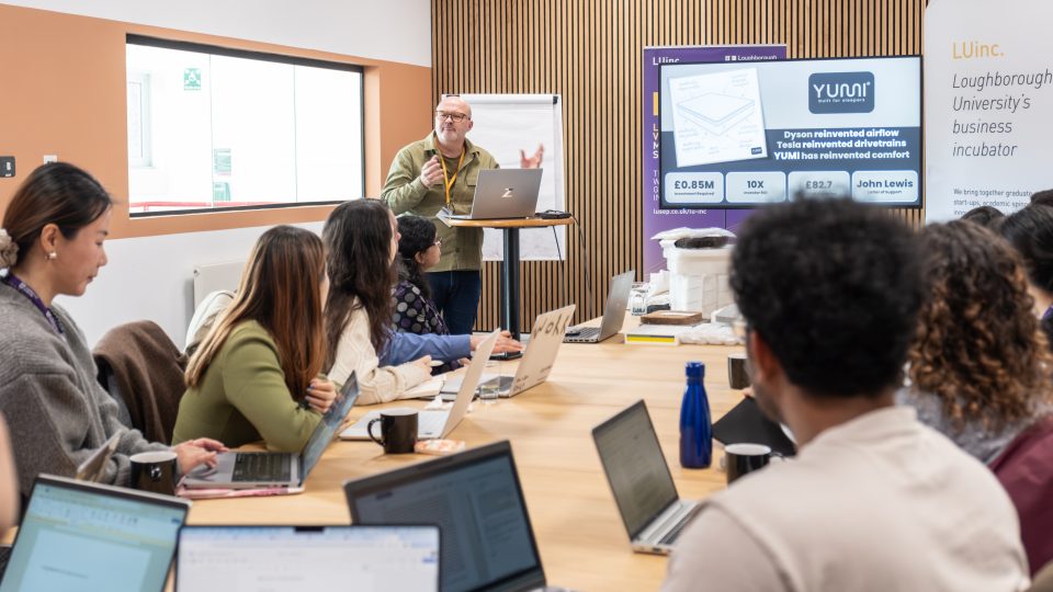 A person giving a presentation to a group sat at a table behind their laptops.