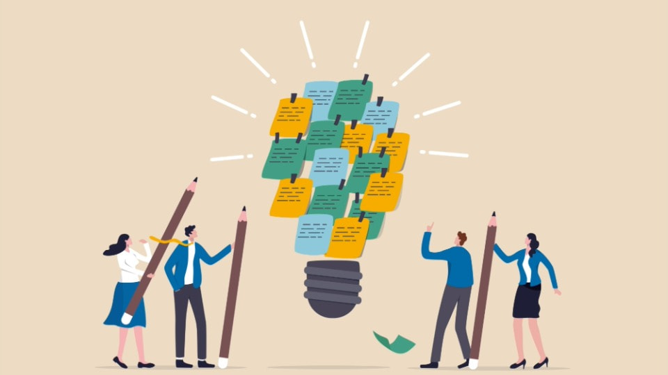 People holding large pencis and looking at a lightbulb made of green, blue and yellow sticky notes