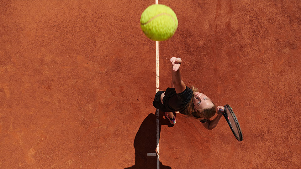 Female tennis player on a clay court serving a ball