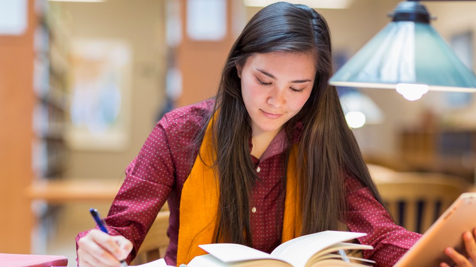 A student studying at a desk, reading a text book.
