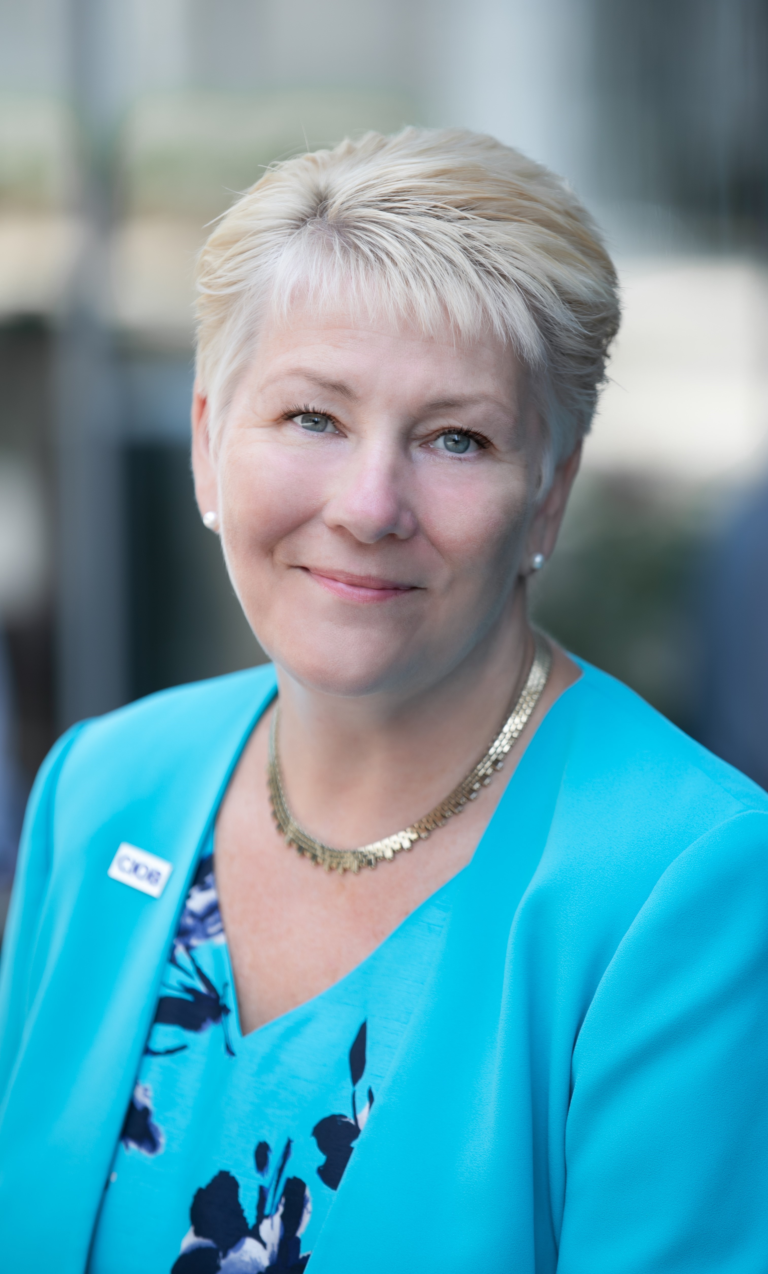 Professional photo of Caroline Gumble, smiling face on at the camera wearing a blue cardi and shirt 