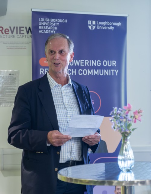 Chris Gill holding a piece of paper and speaking at an event on campus.