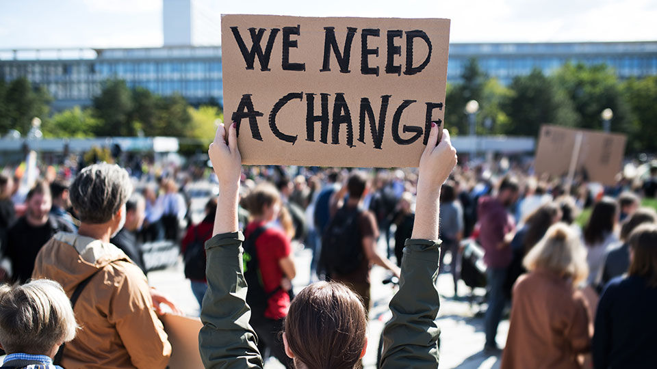 A person standing in a crowd with their back to the camera, holding up a placard that reads 