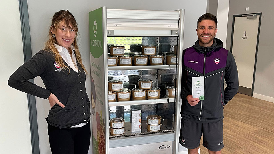 Two colleagues standing next to the Green Bowl fridge in Holywell Fitness Centre