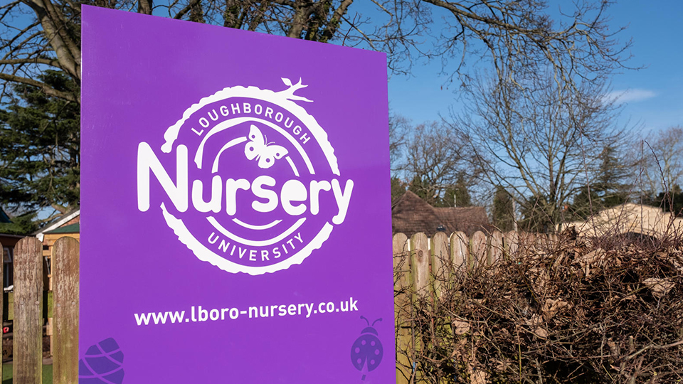 A photo outside the nursery with a purple sign with the Loughborough University Nursery logo on.