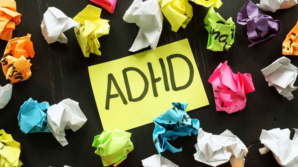 A yellow note with 'ADHD' written on, surrounded by screwed up balls of paper.