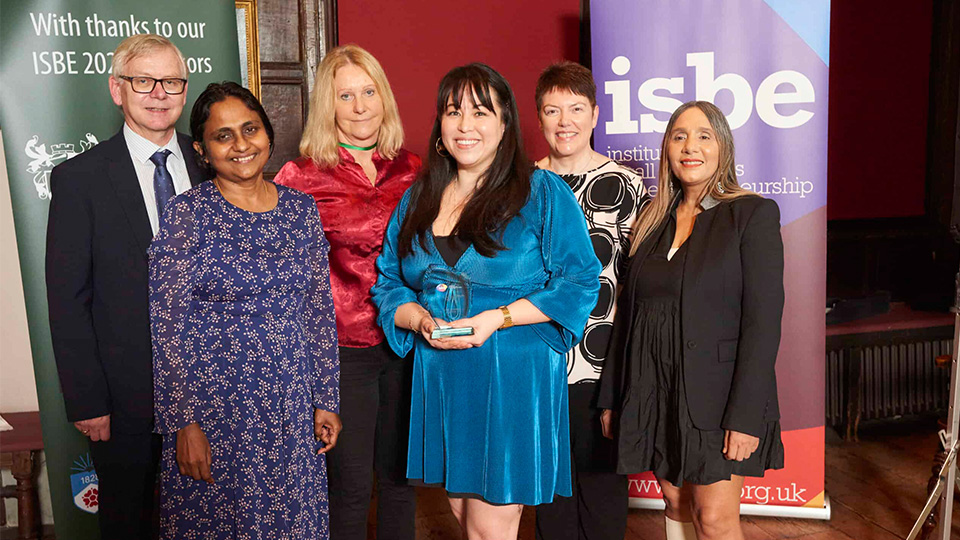A photo of Dr Angela Dy with co-authors of her winning paper at the ISBE Conference Awards, holding a plaque alongside people presenting the award, all stood smiling towards the camera
