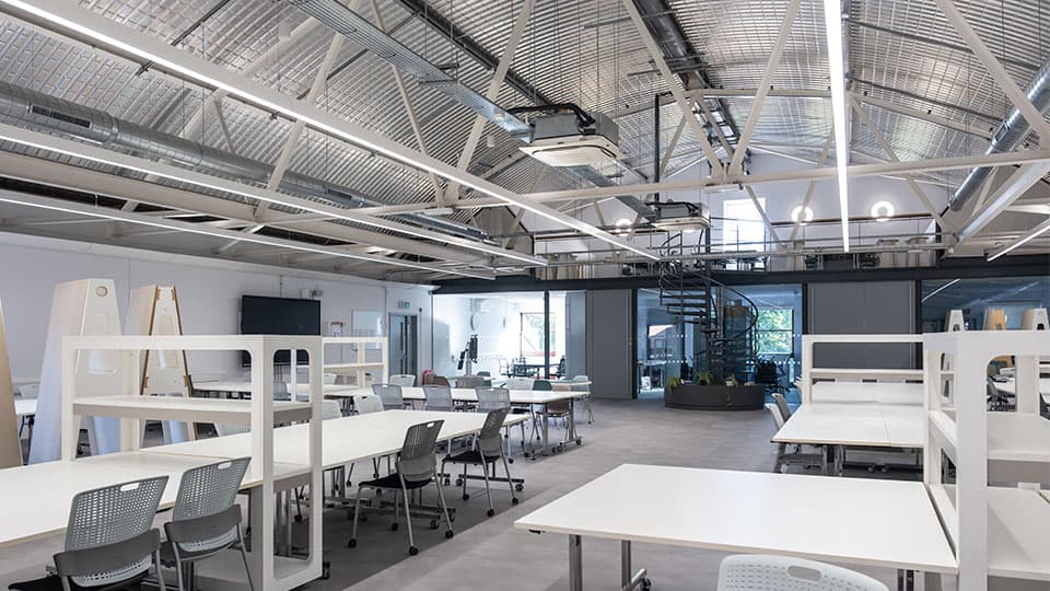 Spacious interior of the new Architecture learning and teaching space in Michael Pearson with white desks lit by bright lighting and a sleek industrial feel