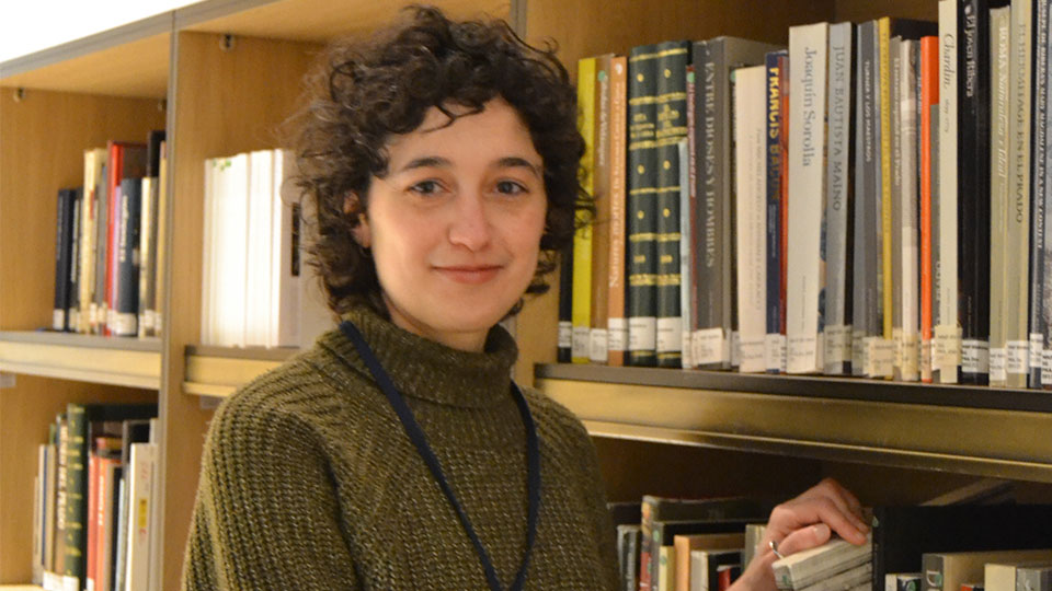 Ana Baeza Ruiz standing in front of stack of books