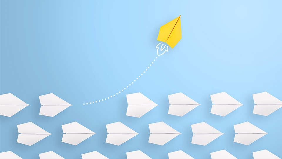 photo of white paper planes on a blue background, with a yellow paper plane soaring into the air