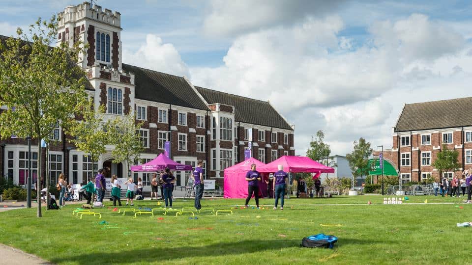 People wearing purple t-shirts and children playing on the grass alongside pink gazebo's in front of Hazlerigg Building on campus.