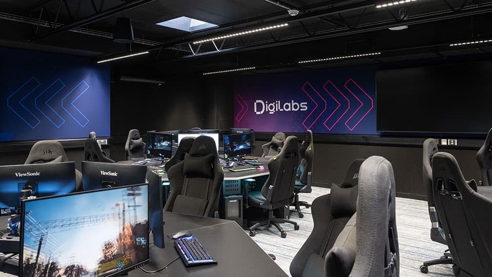 New black gaming style chairs around circular desks  in a modern room with monitors and Digilabs logo in the background