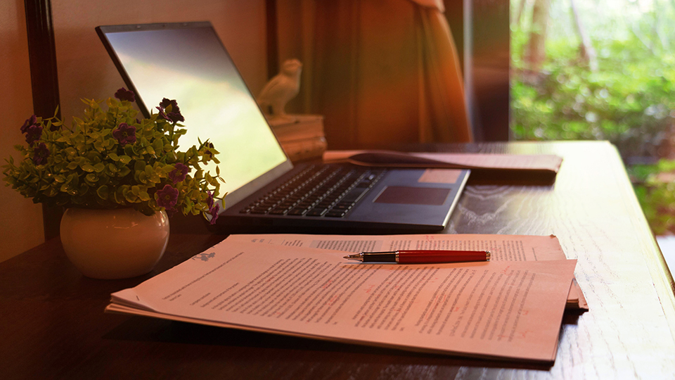 Image of a laptop, papers, a pen, and desk accessories 