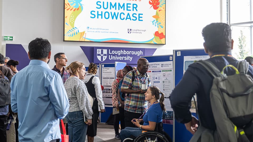 Doctoral Researchers viewing exhibition stands and discussing the showcase with a sign reading 'Summer Showcase' above them