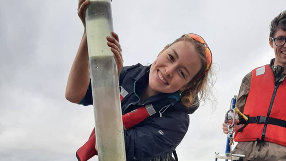 Photo of Savannah smiling at the camera whilst stood on a boat undertaking research