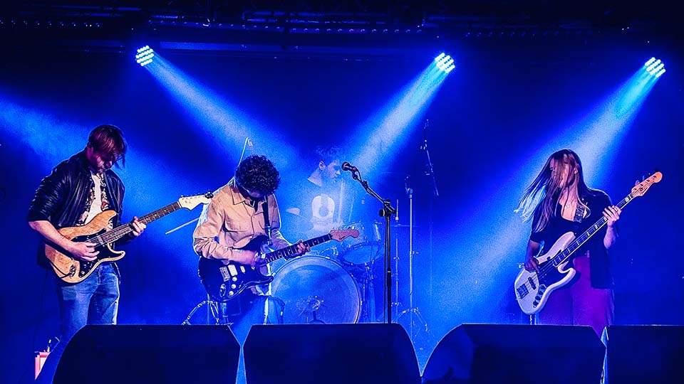 A band of four people playing on stage under blue lighting.