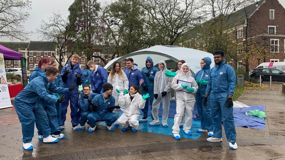A group of people wearing blue and white protective suits, outdoors on a rainy day.