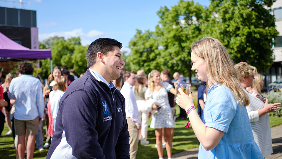 Photo of two students speaking and laughing together outside at the Garden Party event hosted by the University for Hall Committees