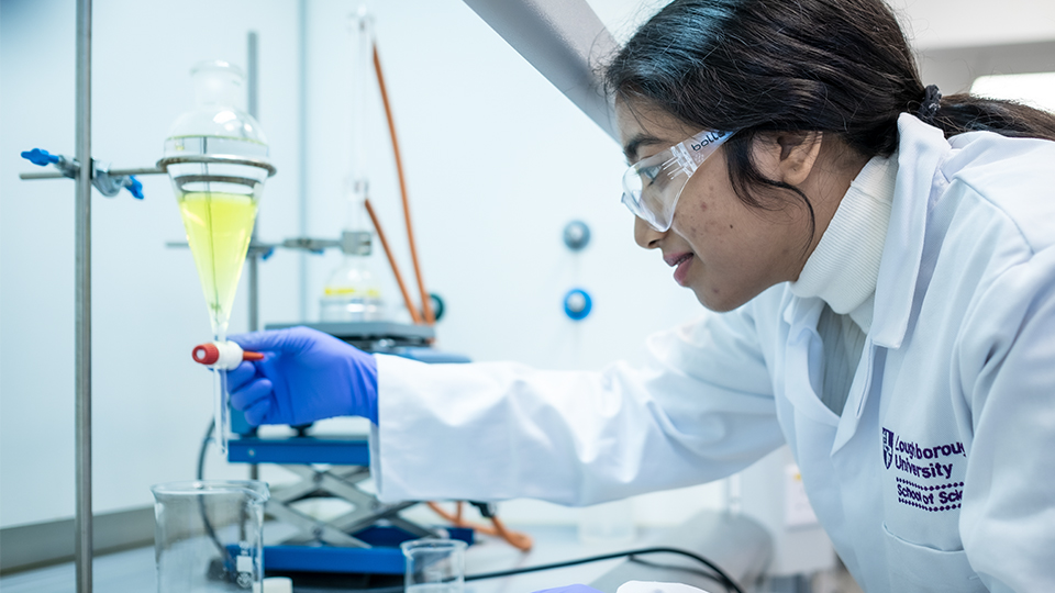 Photo of a woman wearing a Loughborough University lab coat in a lab setting looking down at some research 