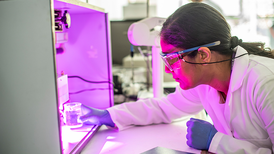 photo of a female student testing something wearing a lab coat and goggles