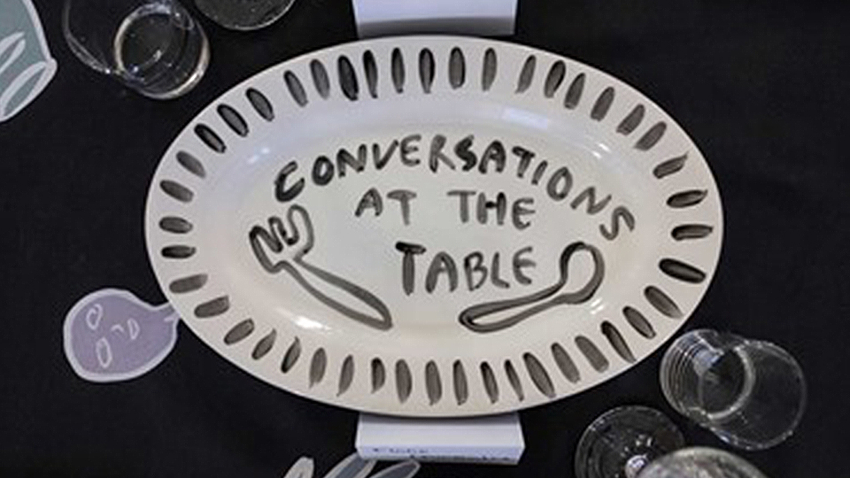 Photo of a painted plate with the words 'Conversations at the Table' glazed on it