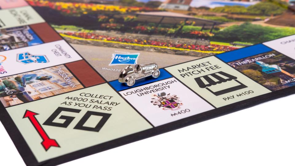 A corner view of the new Loughborough edition Monopoly board, focusing on the Loughborough University tile with a silver car playing piece on the tile. 