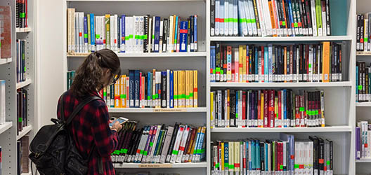 photo of student in the Library stood in front of a shelf of books