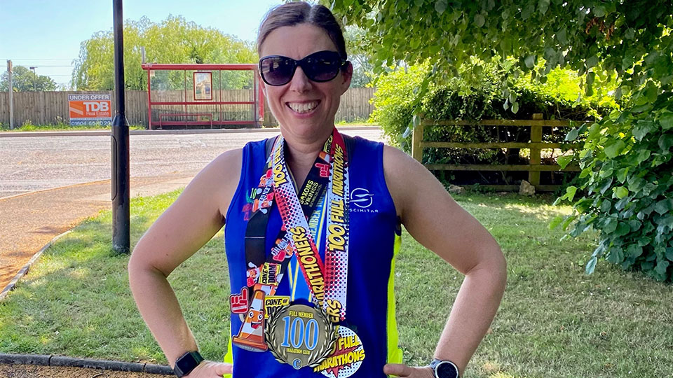 Photo of Professor Liz Peel after her 100th marathon stood outside wearing her medals