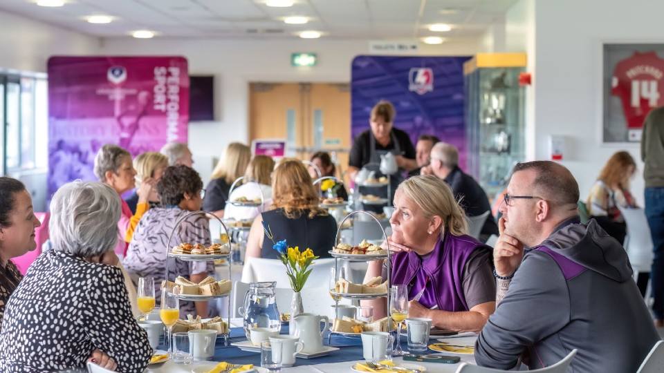 Groups of staff sat around round tables with afternoon tea stands talking to one another at the Holywell Stadium