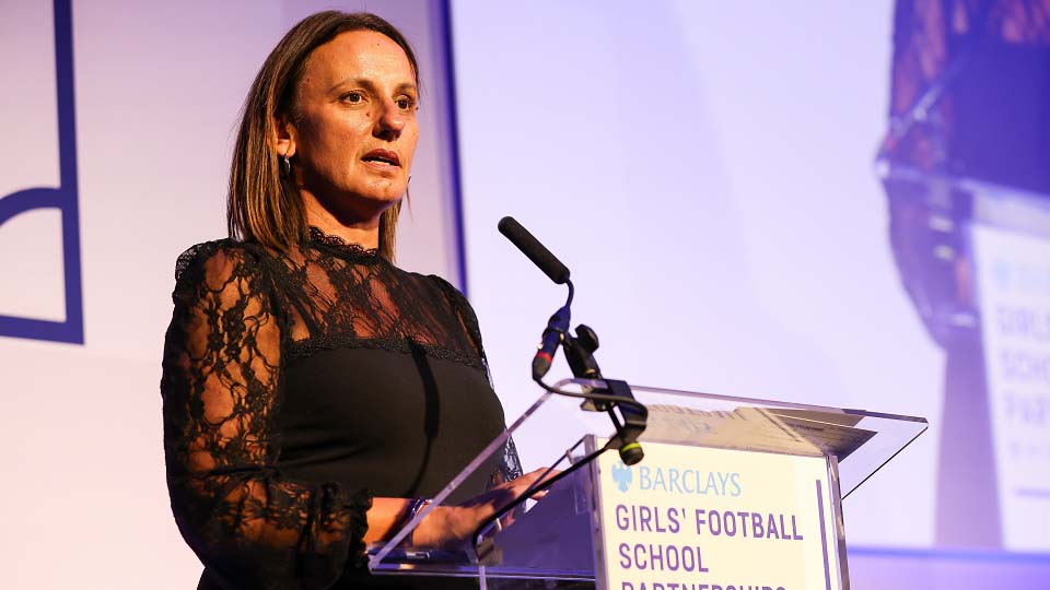 Louise Gear speaking into a microphone on a stage.