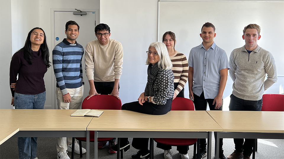 Margaret (Meg) Dawson sat on a table facing the camera, pictured with a group of students from the University 