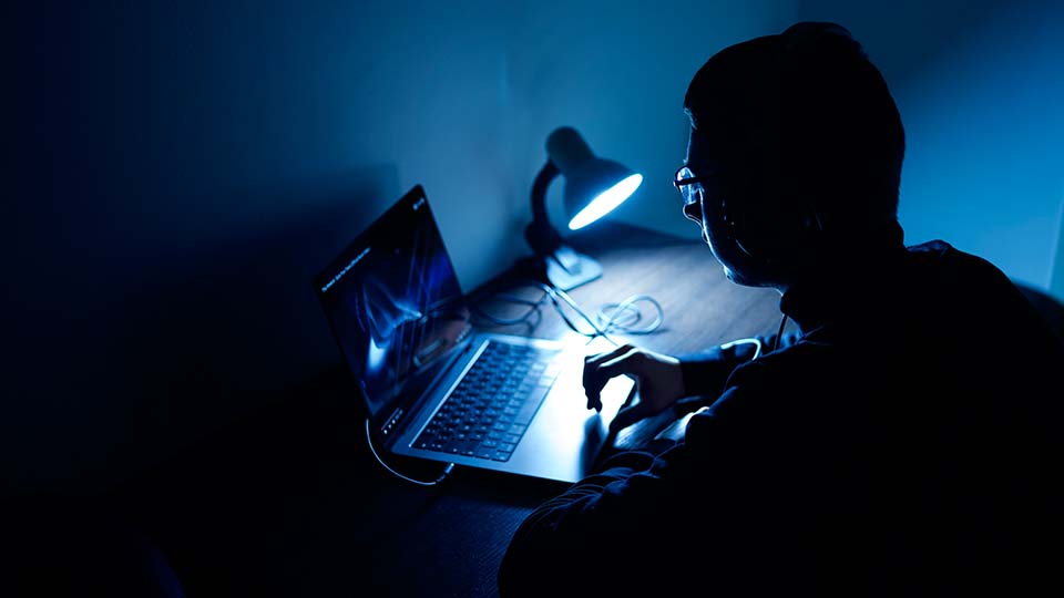 photo of a man sat in a dark room by a laptop