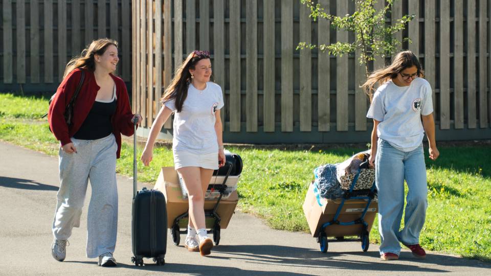 Three students walking through campus during move-in week carrying luggage