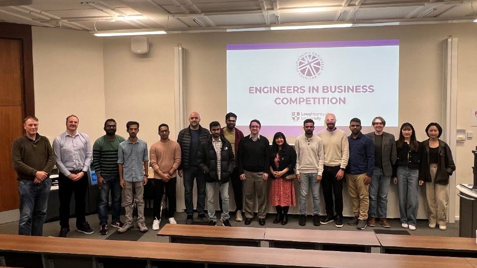 A group of people standing in a row in front of a projection reading 'Engineers in Business Competition' and the Loughborough University logo. 