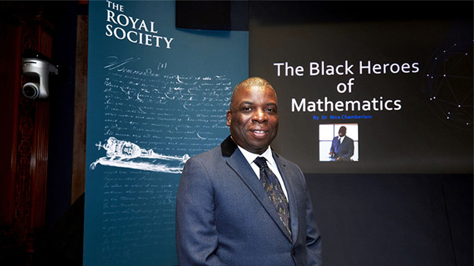 Photo of alumnus Nira Chamberlain, stood in front of a standing banner promoting a previous event he presented