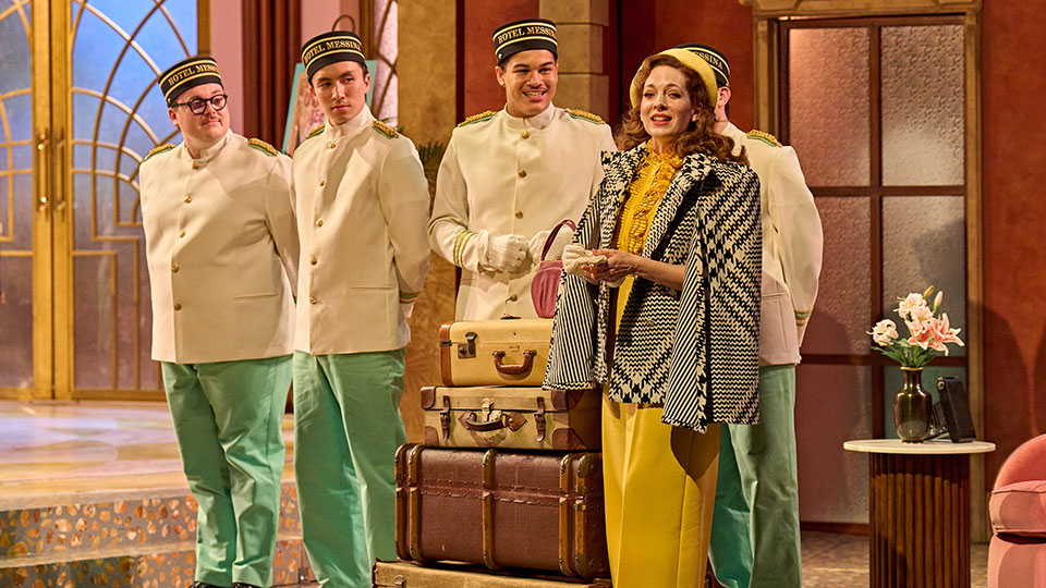 Production still from Much Ado About Nothing - Katherine Parkinson in yellow dress stood with ensemble 