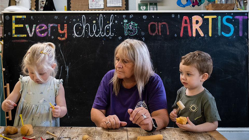 Two children making crafts with a teacher