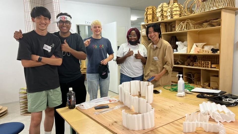 Photo of the five students from Loughborough and Hiroshima Institute of Technology smiling together towards the camera, along with a small scale design of the teahouse on a table in front of them.