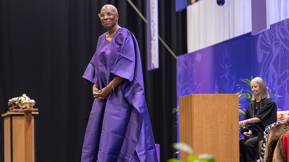 Pauline standing on stage in a purple gown at a graduation ceremony.