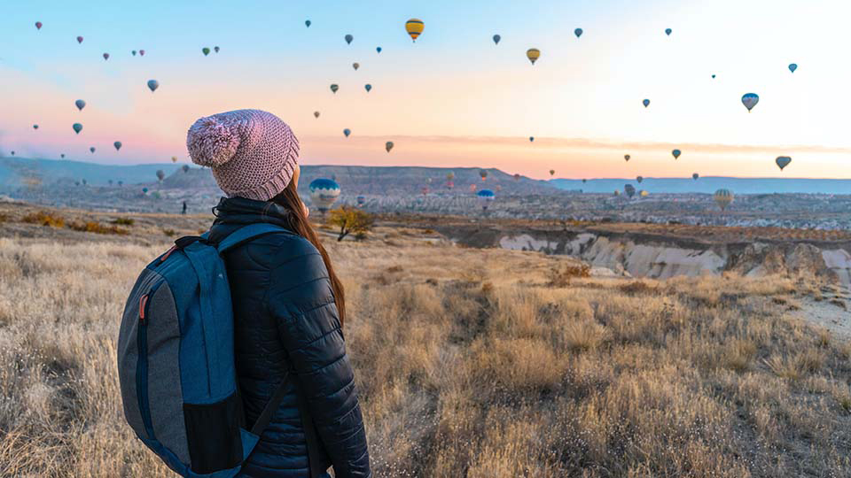 Photo of a girl look out to horizon with mountains and hot air balloons