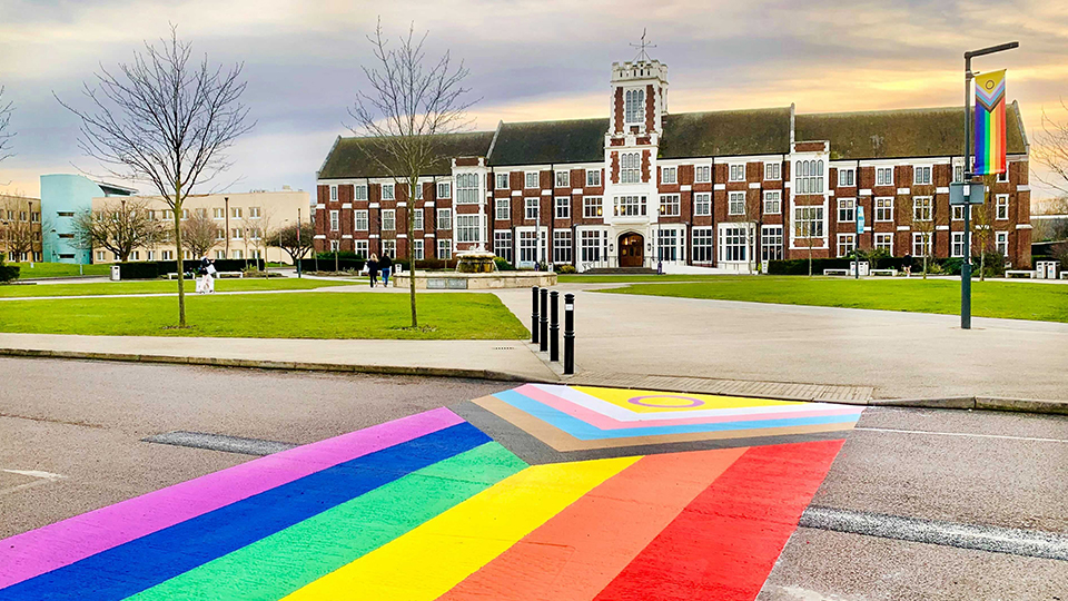 Photo of the Progress Pride installation painting on the road, with the Hazlerigg Building and lawn in the background